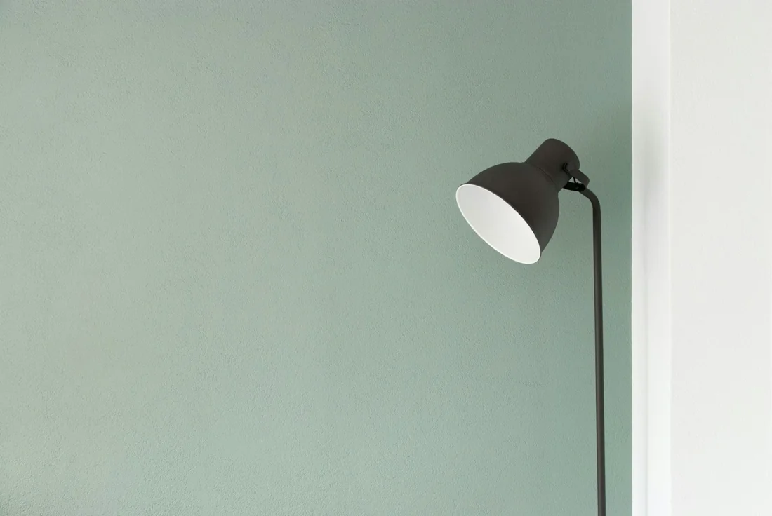 A simple desk lamp against a muted green wall